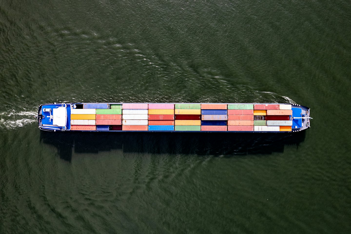 A large cargo ship carries many containers on the dark green water.
