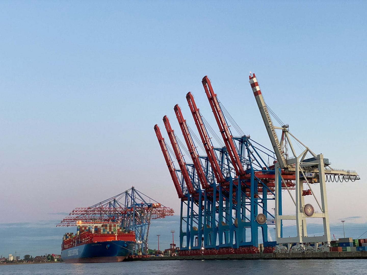 Container ship docked at a busy port with large cranes.